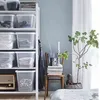 A shelf of storage boxes next to a chair with books and a plant. Voir les images du produit