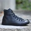 A pair of black leather Converse Chuck Taylor high-top sneakers are shown from the side, resting on a concrete surface with a blurred background. Produktbild-Vorschau