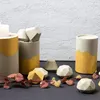 A collection of concrete decorative objects with gold accents, arranged on a dark surface in front of a textured white wall. Produktbild-Vorschau