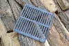 A square metal grate rests on a pile of chopped firewood. Anteprima dell’immagine prodotto
