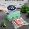 A hand is shown operating a green vacuum sealer machine that is sealing a piece of meat in a plastic bag. Broccoli and herbs are visible in the background. Produktbild-Vorschau