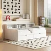 A white daybed with storage drawers is set up in a bedroom with a large abstract artwork on the wall and a floor lamp. Náhled obrázku produktu