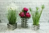 Three decorative vases with artificial plants and flowers are displayed against a white brick wall. Produktbild-Vorschau