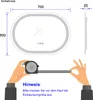 Diagram showing the dimensions of an oval LED bathroom mirror, with a hand holding a measuring tape. Podgląd zdjęcia produktu