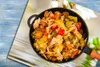 A close-up shot of a pan filled with cooked vegetables, placed on a surface that appears to be a magazine or brochure with a floral design. Náhľad obrázku produktu