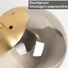 A close-up view of a gold-colored lamp fixture with a smoky gray glass globe. Produktbild-Vorschau