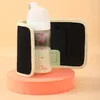 A baby bottle warmer is shown on a pink pedestal against a light peach background. Produktbild-Vorschau