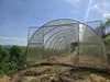 A greenhouse structure on a hillside with a view of rolling hills and trees in the background. Produktbild-Vorschau