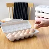 A hand is placing an egg into an open egg holder on a wooden table. Produktbild-Vorschau