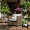 A patio scene with wicker furniture and plants, featuring a black wooden plant stand. Produktbild-Vorschau