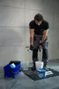 A man is mixing grout with a power drill in a room with tiled walls. Produktbild-Vorschau