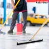 A person is cleaning a floor with a squeegee in what appears to be a garage or workshop, with a yellow truck in the background. Náhled obrázku produktu