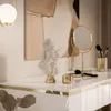 A close-up view of a white console table with gold accents, featuring decorative items like a bust, a makeup mirror, and makeup brushes. Produktbild-Vorschau