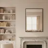 A mirror hangs above a fireplace, reflecting a window with curtains and a sofa. A bookshelf filled with books and decorative items is to the left. Anteprima dell’immagine prodotto
