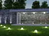 A modern outdoor lighting setup with spherical garden lights illuminating a grassy lawn in front of a stone wall and glass-enclosed building. Náhľad obrázku produktu