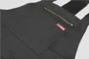 A close-up view of a black cargo overall with a zipper pocket and a red brand label. Produktbild-Vorschau