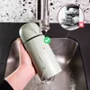 A person is washing a green thermos bottle under a faucet in a sink. An inset image shows a dishwasher with a red cross symbol. Voir les images du produit