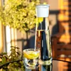 A glass carafe and a glass of water with lemon slices are placed on a reflective surface, with a blurred green plant and wooden furniture in the background. Produktbild-Vorschau
