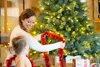 A woman and a child are decorating a Christmas tree with red tinsel. Produktbild-Vorschau