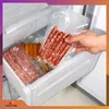 A hand is placing vacuum-sealed sausages into a freezer drawer, alongside vacuum-sealed bacon and hot dogs. Podgląd zdjęcia produktu
