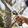 A hand holding a Fiskars folding saw and cutting a tree branch. Produktbild-Vorschau