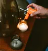 A hand holding an orange lighter near a candle. Produktbild-Vorschau