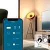 A smartphone app interface is shown in the foreground, displaying controls for a smart home device. In the background, a modern living room scene features a TV, a floor lamp, and a speaker. Produktbild-Vorschau