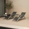 Two dark gray lounge chairs and a small side table are set up on a light-colored gravel patio next to a small tree. Voir les images du produit