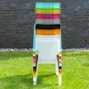A stack of colorful plastic chairs on a grassy lawn in front of a brick wall. Produktbild-Vorschau