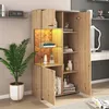 A vitrine cabinet with open doors, displaying decorative items and books, in a room setting with a plant and a desk in the background. Voir les images du produit