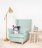 A plush toy is placed on a teal armchair next to two small side tables. A floor lamp is to the left of the armchair. Voir les images du produit