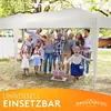 A family and friends are gathered under a white pop-up tent in a backyard, celebrating an event. There are decorations and gifts present. Produktbild-Vorschau
