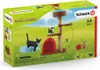 The image shows the packaging for a Schleich Farm World cat playset, featuring toy cats, a cat tree, and a small house, set against a grassy, outdoor backdrop. Podgląd zdjęcia produktu