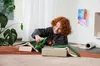 A young boy is playing with a toy monster truck on a rug, surrounded by books. Produktbild-Vorschau