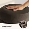 A hand is pressing down on a round, brown cushion, demonstrating its softness. A close-up of the fabric texture is shown in a circular inset. Produktbild-Vorschau