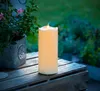 An LED candle sits on a wooden surface next to a potted plant. Produktbild-Vorschau