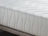A close-up view of a white mattress with a textured surface and wavy stitching. Produktbild-Vorschau