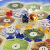A close-up view of a board game, likely Settlers of Catan, with game pieces and dice on the board. Náhľad obrázku produktu