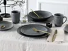 A table setting with dark gray stoneware plates, bowls, and mugs, accented with gold cutlery and a glass of water. Náhľad obrázku produktu