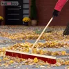 A person is sweeping fallen leaves on a paved walkway with a broom. Náhled obrázku produktu