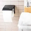 A toilet paper holder with a roll of toilet paper attached, mounted on a tiled wall. Produktbild-Vorschau