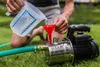 A person is pouring water into a garden pump using a measuring jug and a funnel. Produktbild-Vorschau