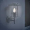 A wall-mounted outdoor lamp with a glass shade and a metal frame, illuminated by a single bulb. Produktbild-Vorschau