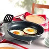 A table setting with a frying pan containing two fried eggs, a spatula, a wooden plate, and glasses of red liquid. Produktbild-Vorschau
