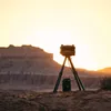 A portable pizza oven on a tripod is set up on a rocky outcrop overlooking a canyon at sunset. Produktbild-Vorschau