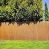 A woven reed fence is shown in front of green trees and a green lawn. Podgląd zdjęcia produktu