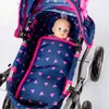 A doll is sitting in a doll stroller with a navy blue and pink triangle pattern. Produktbild-Vorschau