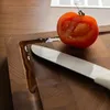 A close-up shot of a tomato half and a knife on a wooden cutting board. Produktbild-Vorschau