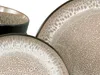 A close-up view of stoneware plates and a bowl with a speckled beige and white pattern. Produktbild-Vorschau