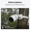 A white security camera mounted on a tree trunk during a rain shower. Produktbild-Vorschau